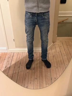Blå skinny jeans från Levis - Säljer ett par blå Levis jeans med skinny passform och klassisk femficksdesign. Jeansen har en snygg tvätt med slitningar och är tillverkade i jeansmaterial. De har låg midja och smal siluett som sitter tajt längs benen.