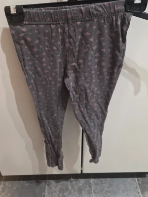 Grå leggings med rosa hjärtan från bonprix  - Snygga grå leggings från bonprix med gulligt rosa hjärtmönster över hela byxan. Mjukt och stretchigt material med resår i midjan för skön passform. Perfekta att matcha med en oversized hoodie eller t-shirt.