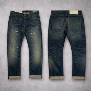 Blå selvedge jeans - Snygga blå jeans från Levi's med coola slitningar och uppvikta benslut. Jeansen har klassisk femficksdesign och en mörk tvätt med ljusare partier framtill och baktill. Materialet är robust denim och passformen är rak med normal midja.Dem är 78 cm midja och ca 100 cm långa. 