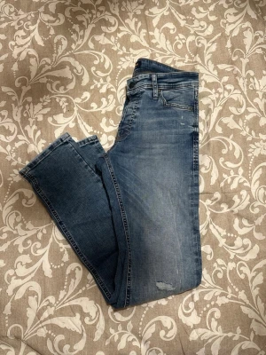 Slim Glenn jeans från Jack & Jones - Säljer ett par blå Slim Glenn jeans från Jack & Jones i storlek 29/32. Jeansen har en slim passform, klassisk femficksdesign och snygga slitningar på benen. Materialet är mjukt denim i bomull med lite stretch för extra komfort.