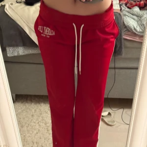 Röda mjukisbyxor från Bershka - Säljer ett par röda mjukisbyxor/träningsbyxor från Bershka med vita sidoränder och snörning i midjan. Byxorna har en loose passform och elastisk midja och inuti är det flismaterial. Perfekta för chill dagar, dans eller träning och har tryck med 'Academy Life' på framsidan. Superbekväma och snygga! De är nyskick o jag har använt de 1- 2 gånger. ❣️går att bära lowwaist och highwaist.