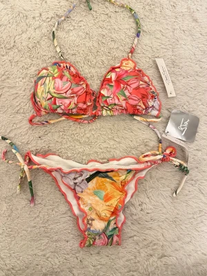 Blommig bikini - Färgglad bikini från Costa Troppical med blommigt mönster och scrunch i rumpan! Aldrig använd, storlek M men passa bra på mig som bär XS!☺️💗
