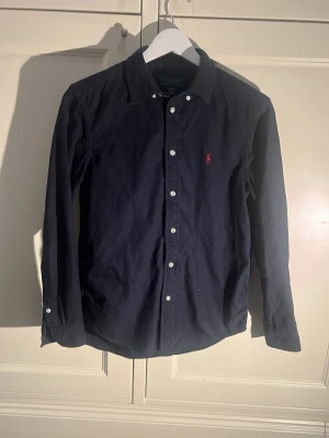 Ralph Lauren skjorta - En mörkblå Ralph lauren skjorta med en röd logga. Den är L i barn (14-16) Riktigt fint skick.