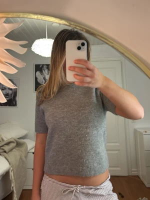 Grå stickad kortärmad tröja från Zara - Supermjuk grå stickad tröja från Zara i storlek M. Tröjan har korta ärmar, rund halsringning och ribbade kanter. Perfekt att styla med jeans eller kjol för en chill look.