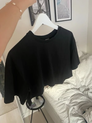 Svart croppad t-shirt - Enkel svart croppad t-shirt med rund hals och korta ärmar. Oversized fit och är i mjuk bomull. Den är aldrig använd och lappen är på. Hör av er för fler frågor💗💗