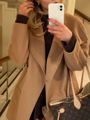 Beige kappa med bred krage - Säljer en snygg beige kappa med bred krage och stilren design. Jackan har en rak passform och stora fickor framtill. Materialet är mjukt och känns lyxigt, perfekt för dig som vill ha en klassisk look med modern touch.