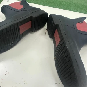 Svarta Tretorn chelsea boots med röd resår - Säljer ett par svarta chelsea boots från Tretorn med röd resår på sidorna. Skorna har platt sula och är tillverkade i syntetmaterial som tål regn. Perfekt för dig som vill ha stilrena boots med färgdetalj och enkel att dra på tack vare resåren.