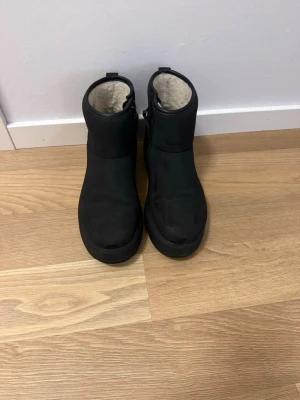 Svarta boots med pälsfoder - Säljer ett par svarta boots med rund tå och platt sula. Insidan är fodrad med mjuk päls som håller fötterna varma under kalla dagar. Utsidan är i mocka och de har en enkel, stilren design som passar till många outfits.