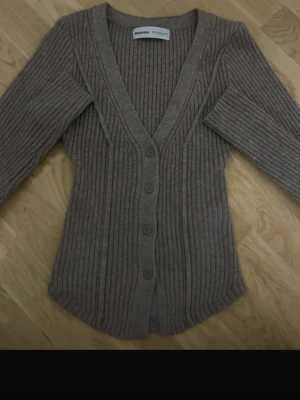 Beige ribbad kofta från Bershka - Säljer en beige/brun ribbad kofta från Bershka i storlek XS. Koftan har v-ringning, långa ärmar och knappar framtill. Den är figurnära och gjord i ett mjukt stickat material som är perfekt för lager-på-lager under hösten och vintern.