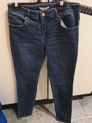 Mörkblå skinny jeans från H&M, strl 36 - Snygga mörkblå skinny jeans från H&M i storlek 36. Klassisk femficksmodell med knapp och dragkedja framtill. Materialet är 66% bomull, 30% polyester, 3% viskos och 1% elastan för en bekväm och stretchig passform. Perfekt till sneakers eller boots.