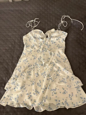 Blommig kortklänning med volanger - Supersöt kortklänning, den har vit ”lining” på insidan så den är inte genomskinlig, storlek M men den är mer som en S