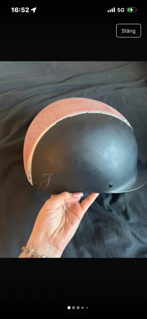 Svart och rosa ridhjälm med glitter - Säljer en snygg ridhjälm i svart med en glittrig rosa panel på ovansidan och silverfärgade detaljer. Hjälmen har en klassisk form med skärm framtill och ventilationshål på sidorna. Perfekt för dig som vill sticka ut i stallet!