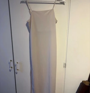 Beige långklänning från H&M - Säljer en stilren beige långklänning från H&M i storlek XS. Klänningen har smala axelband, rak passform och en slits på sidan. Köpt för länge sedan men knappt använd 