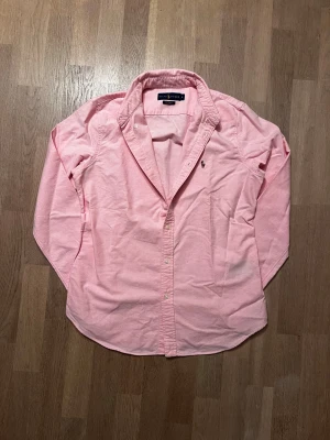 Rosa skjorta från Ralph Lauren - Snygg rosa skjorta från Ralph Lauren med lång ärm. Klassisk, tidlös design som är perfekt att bära till både vardags och finare tillfällen. 👕 Personen på bilden är cirka 183 🙌  Skick 9/10 ✅. Nypris cirka 1700.  Skickar alltid inom 24 timmar med tanke med julafton 🎄 🚚
