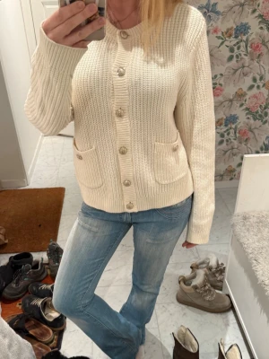 Söt vit stickad kofta med guldknappar - Stickad kofta med guldknappar och fickor. Krämvit färg 
