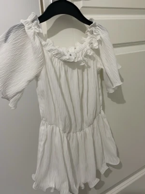 Vit topp från Missguided Petite - Supersöt vit topp från Missguided Petite i storlek 34. Den har volangdetaljer vid halsringningen och ärmarna, samt en rynkad struktur i ett lätt och luftigt material. Perfekt för flera tillfällen