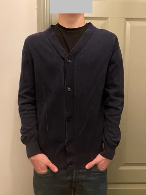 Marinblå kofta/cardigan från A.P.C.  - Riktigt snygg marinblå kofta från A.P.C. i storlek M. Koftan har v-ringning, knappar framtill och ribbade muddar vid ärmslut och nederkant. Koftan är lite urtvättad men fortfarande ett tåligt material. Vid funderingar, fråga på! 