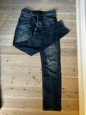 Blå jeans från Neuw - Säljer ett par klassiska blå jeans från Neuw Stockholm med snygg tvätt och raka ben. Jeansen har fem fickor, knappgylf och detaljerade sömmar. Materialet är slitstarkt denim i bomull och passformen är normal. Perfekt för dig som gillar stilrena och tidlösa jeans. Skick: 8/10. Nypris: 1499kr