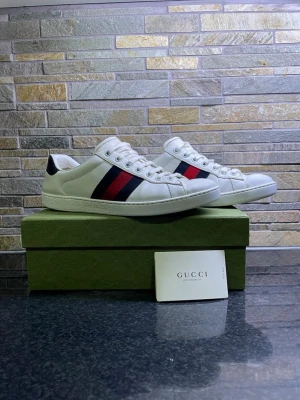 Gucci ace - Säljer ett par snygga Gucci ace sneakers i storlek 42 men kan även passa 43 med klassiska ränder i rött och mörkblått på sidan. Hälpartiet är svart med textur och Gucci-logga. Tillverkade i skinn för en lyxig känsla.