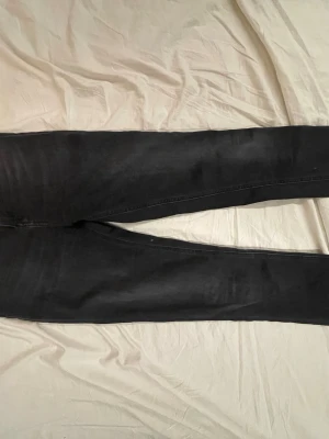 Svarta jeans från Nudie Jeans Co - Säljer ett par svarta jeans från Nudie Jeans Co med klassisk femficksdesign och diskreta sömmar på bakfickorna. Jeansen har hög midja och raka ben, tillverkade i mjukt jeansmaterial. Perfekta för dig som gillar en clean och stilren look. Pris kan diskuteras vid smidig affär