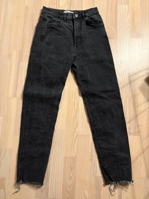 Svarta jeans från Pull&Bear, strl 36 - Svarta jeans från Pull&Bear i storlek 36. Modellen har medel hög midja, raka ben och råa, fransiga benslut för en cool vibe. Klassisk femficksdesign och knappgylf. Materialet är jeans med en mörk tvätt som ger en snygg look.