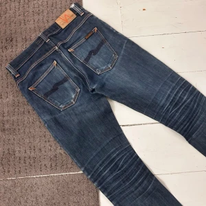 Mörkblåa Nudie Grim Tim Jeans - Riktigt snygga Nudie Jeans i Grim Tim | W30 L32 | Nypris 1699kr | Riktigt fint skick, förutom en diskret slitning under ena knäet. | Midja: 37-40cm (Stretch) längd: 100cm | Tydliga fades, tydliga honeycombs & whiskers. | Skriv vid minsta fundering, pris ej hugget i sten! 