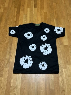 Svart t-shirt med vita tryck från Denims - Cool svart t-shirt från Denims med unika vita cirkelformade tryck över hela plagget, både fram och bak samt på ärmarna. Klassisk passform med rund hals och korta ärmar. Perfekt för dig som vill sticka ut med en grafisk look.