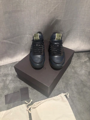 Valentino Rockrunner sneakers blå - Säljer ett par snygga Valentino Rockrunner sneakers i mörkblått skinn och mocka med svarta snören och coola pyramidnitar på sidorna. Beige sula med mönster och guldiga detaljer på plösen. Kommer med originalkartong och dustbags. Säljer för 1999 för allt og är med men det sulan är förstörd. Kom med frågor 