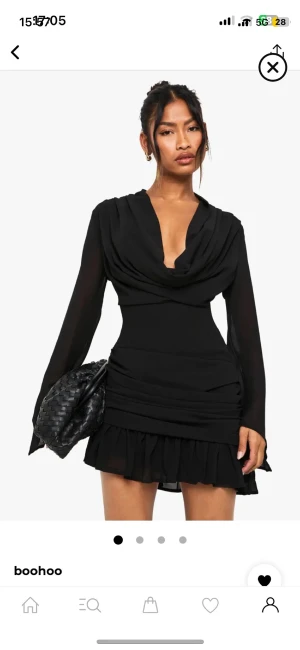 Svart kort klänning från Boohoo - Supersnygg svart kort klänning från Boohoo med draperad v-ringad hals och långa, transparenta ärmar. Kjolen har volangkant och klänningen sitter tight med markerad midja. Perfekt för dig som gillar trendiga detaljer och stilren look.OBS! Helt ny säljer den pga av att den inte passar mig