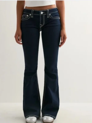 True religion  Mörkblå bootcut jeans med kontrastsömmar - Snygga mörkblå jeans från True Religion med tydliga vita kontrastsömmar och bootcut passform. Lågmidjade med klassiska fickor och ikoniska broderade detaljer på bakfickorna. Tillverkade i jeansmaterial med stretch för skön passform. Inköpta för 1599.