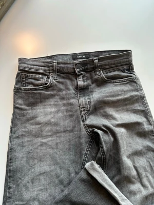 Grå Replay jeans straight fit modell Thad 158 cm 14 år - Säljer ett par gråa Replay jeans med klassisk femficksdesign och raka ben. Jeansen har snygga slitningar och detaljerade bakfickor med Replay-logga på linningen. Perfekta för dig som gillar en enkel men stilren look.