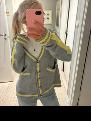  Zara kofta  - Säljer en mysig grå kofta med gula ränder och knappar framtill. Koftan har två fickor och ribbade muddar. Perfekt att slänga på sig över en t-shirt för en chill look.