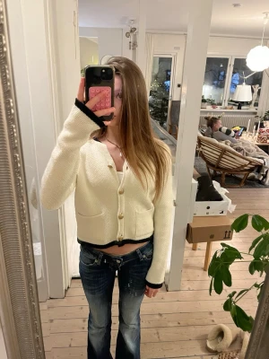 Vit kofta med svarta detaljer och guldknappar - Säljer en söt, vit kofta med svarta detaljer vid ärmslut och nederkant. Koftan har guldiga knappar framtill och två fickor. Den är stickad och har lite tjockare material💙