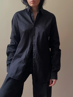 Vintage Black Cotton Emmanuelle Khanh Shirt - Vintage Black Cotton EK by Emanuelle Khanh Shirt. Excellent Condition. Collared shirt with Black buttons. Original Tagged Size Men's L, slim Fit. Model is 160cm (5”3) and generally fits S/M. 100% cotton.   70 CM/ 27.6 IN Length  67 CM/ 26.4 IN Sleeve  44 CM/ 17.3 IN Shoulders 96 CM/ 37.8 IN Chest 