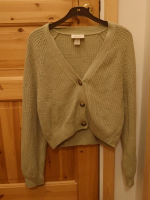 Ljusgrön kofta  - Säljer en ljusgrön stickad kofta från Monki med v-ringning och tre stora knappar framtill. Koftan har lång ärm och ribbade muddar vid ärmslut och nederkant.☺️💕