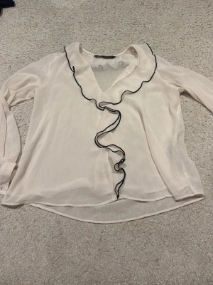 Vit/svart blus från zara - En beige/vit blus med volanger med svarta detaljer på 