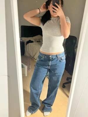 Blå wide jeans från gina tricot  - Säljer ett par blåa jeans från gina tricot med klassisk femficksdesign och bred passform. Jeansen har typ låg  midja, raka ben och en snygg läderpatch bak i midjan. Perfekta för en avslappnad och trendig look.