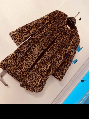 Leopardmönstrad pälsjacka - Säljer en fluffig och trendig pälsjacka med leopardmönster. Jackan har en rak passform, långa ärmar och stängs framtill. Perfekt för dig som vill sticka ut och hålla dig varm under kyliga dagar.