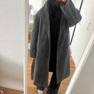 Grå ullkappa från 157, storlek M - Säljer en lång, mörkgrå kappa från 157 i storlek M. Kappan har dubbelknäppning med stora knappar, klassisk krage och raka ärmar.  Perfekt för höst och vinter! Aldrig använd 