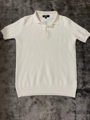 Fendi pike - Säljer en stilren vit henley från Fendi med diskret strukturmönster i tyget. Skjortan har korta ärmar, klassisk krage och knappar framtill. Perfekt för dig som gillar exklusiva och minimalistiska plagg med lyxig känsla.