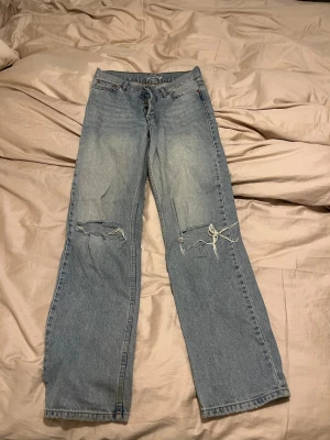 Junkyard Nevermind jeans ljusblå 27 - Ljusblå jeans från Junkyard, modell Nevermind, med raka ben och slitna detaljer vid knäna. Klassisk femficksdesign och normal passform. Jeansen är tillverkade i denim och har en avslappnad vibe.