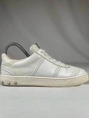 Valentino Garavani vita sneakers - Snygga vita sneakers från Valentino Garavani i skinn med klassisk snörning och coola nitar på sulan. Låg modell med rund tå och diskret logga på plösen. Skorna har en stilren design och kommer med original dustbag.