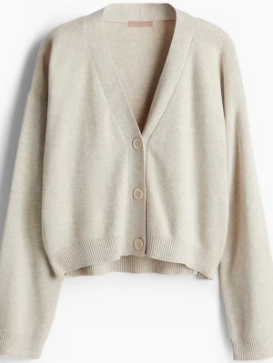 Beige croppad kofta från H&M - Säljer en beige croppad kofta från H&M med v-ringning och stora knappar framtill. Koftan har lång ärm och ribbade muddar vid ärmslut och nederkant. 