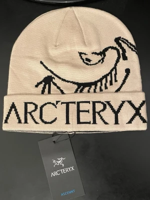 Arc’teryx Ascent Beanie – Beige – Aldrig använt!!! -  Arc’teryx Ascent Beanie – Beige – Aldrig använt!  En stilren och funktionell mössa från Arc’teryx i beige med det klassiska logotrycket. Tillverkad i mjukt och slitstarkt material som håller dig varm både till vardags och vid utomhusaktiviteter. Aldrig använt, taggen sitter fortfarande kvar.  Arc’teryx Ascent Beanie – Beige – Never worn!  