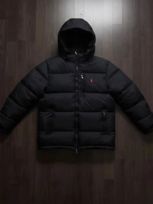 Svart pufferjacka från Polo Ralph Lauren - Säljer en svart pufferjacka från Polo Ralph Lauren i storlek M. Jackan har huva, dragkedja framtill och två sidofickor med dragkedja. Klassisk röd Polo-logga på bröstet och quiltad design som håller värmen under kalla dagar.