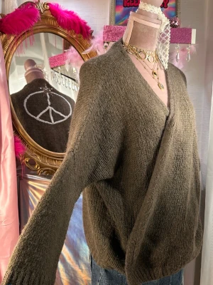 Brun glittrande stickad kofta med peacemärke - Mysig brun stickad kofta med öppen front och lång ärm. På ryggen finns ett stort broderat peacemärke i vitt med en glittrig stjärna upptill. Perfekt för lager på lager och ger en chill vibe till din outfit.