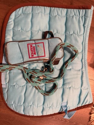 Ljusblå schabrak i storlek FULL+benlindor+grimskaft - Säljer ett schabrak med bruna kanter och vita insidor. Får med matchande benlindor samt grimskaft. Schabraket har ett klassiskt rutmönster och är tillverkad i mjukt syntetmaterial. Perfekt för dig som gillar stilrena detaljer till ridningen. Defekter på varorna syns på bilderna. 