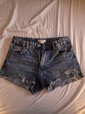 Blå jeansshorts från Gina Tricot - Säljer ett par blå jeansshorts från Gina Tricot med slitna detaljer framtil som inte kommer till användning längre!