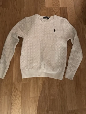 Vit kabelstickad tröja Polo Ralph Lauren - Kabelstickad vit tröja från Polo Ralph Lauren med klassisk rund halsringning och broderad logga på bröstet. Långärmad modell i mjuk bomull som passar perfekt till både jeans och kjol. Enkel men ändå riktigt snygg och tidlös. Storlek L i barn storlek passar 152-161