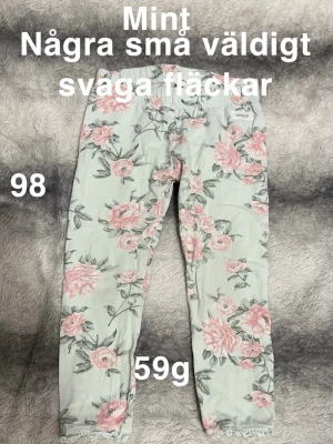 Mintgröna blommiga leggings  - Supersöta mintgröna leggings från Newbie med rosa och gröna blommor över hela byxan. Mjuk resår i midjan och spetsdetalj längst ner vid bensluten. Perfekta för dig som gillar färg och mönster!🌸Svaga fläckar. Storlek 98
